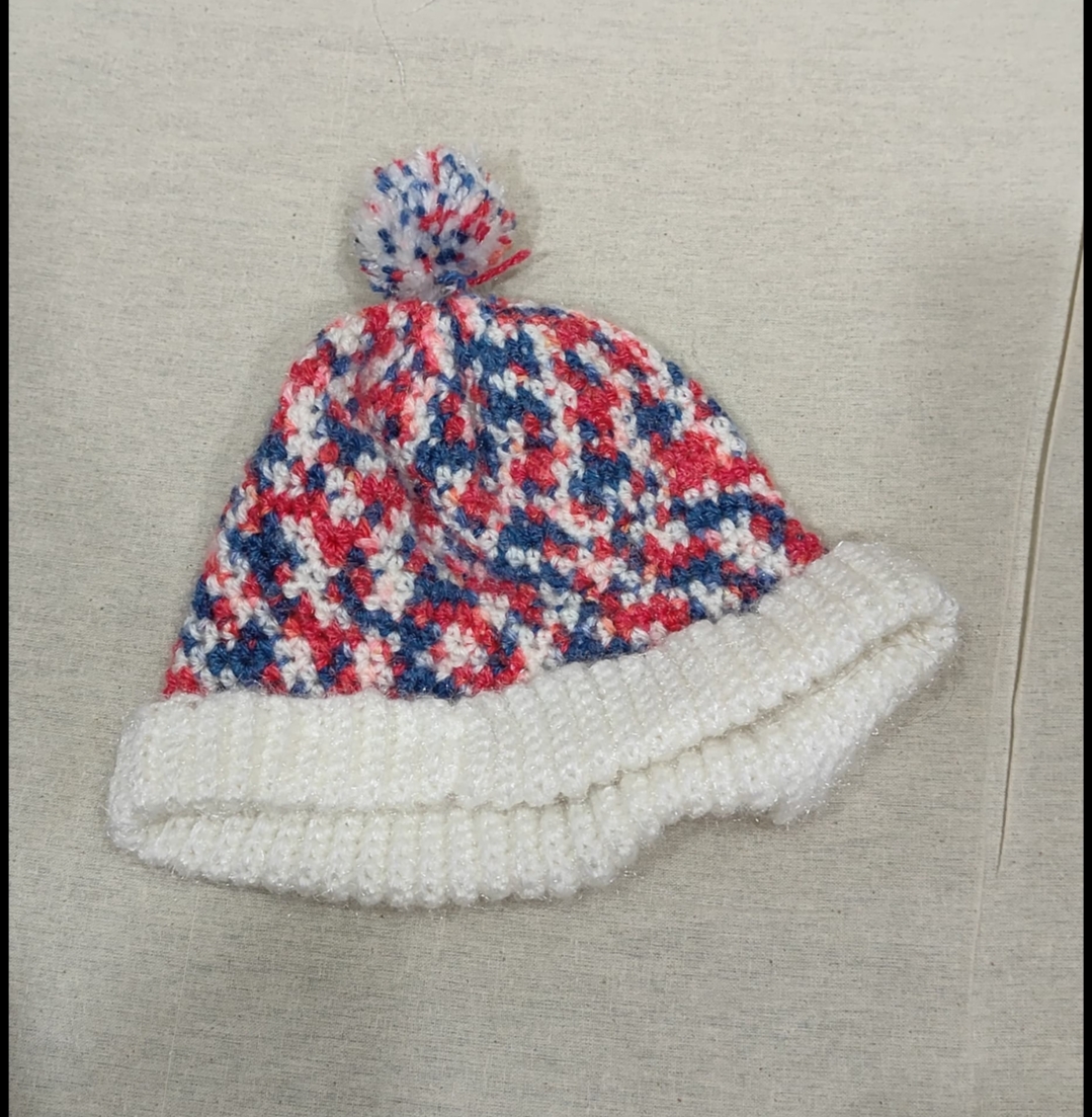 Confetti Pom Beanie — a speckled red, blue and white crocheted beanie with a white folded cuff and matching pom-pom