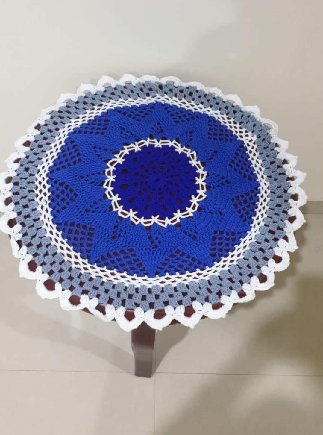 Star Doily — a cobalt blue, grey and white crocheted round doily with a scalloped edge, on a wooden table